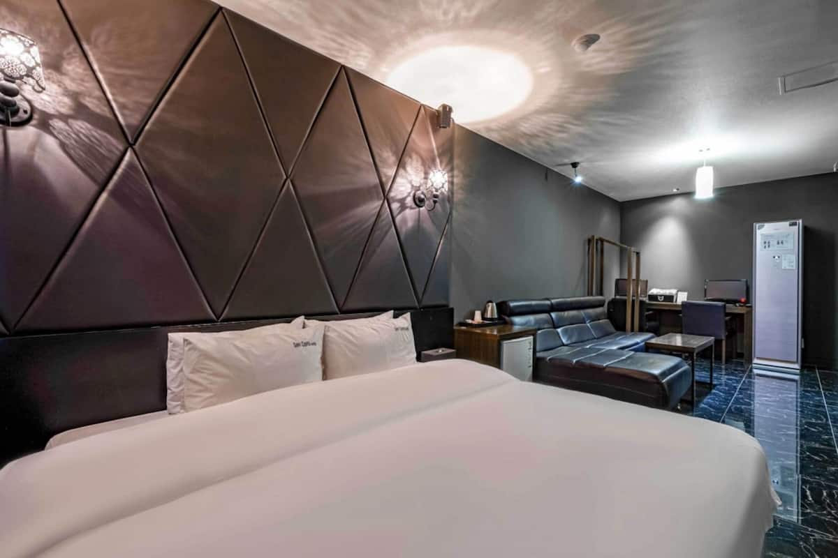 Hotellihuone, jossa on suuri sänky, sohva, työpöytä tietokoneella ja jääkaappi.