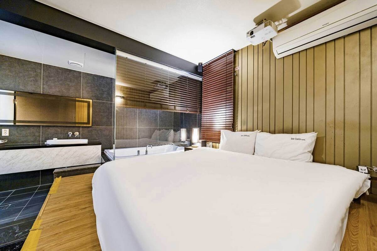 Moderni hotellihuone, jossa on suuri sänky, kylpyhuone peilillä ja pesualtaalla sekä puupanelilla verhoiltu seinä.