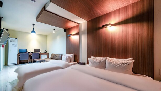 A hotel room with two beds, a desk with a computer, and a refrigerator.