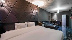 A modern hotel room with a large bed, a sofa, a desk, and a refrigerator.