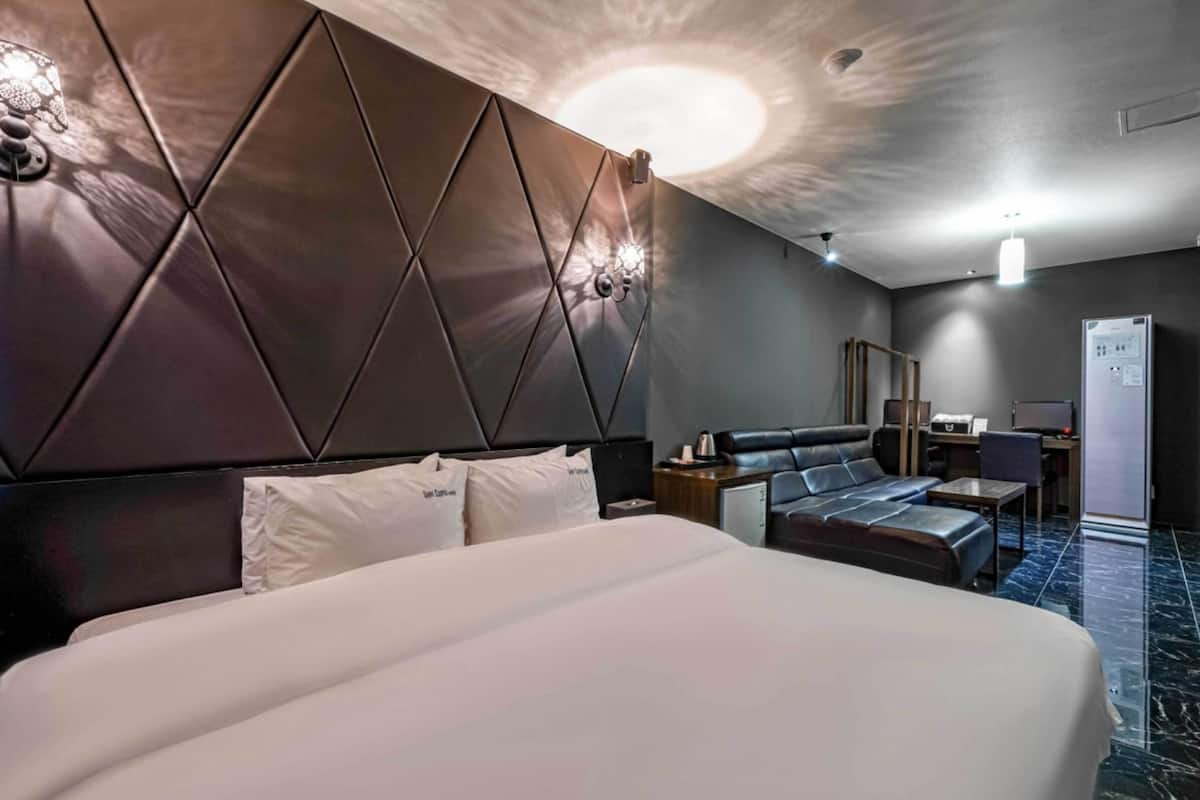 Moderni hotellihuone, jossa on suuri sänky, sohva, työpöytä ja jääkaappi.