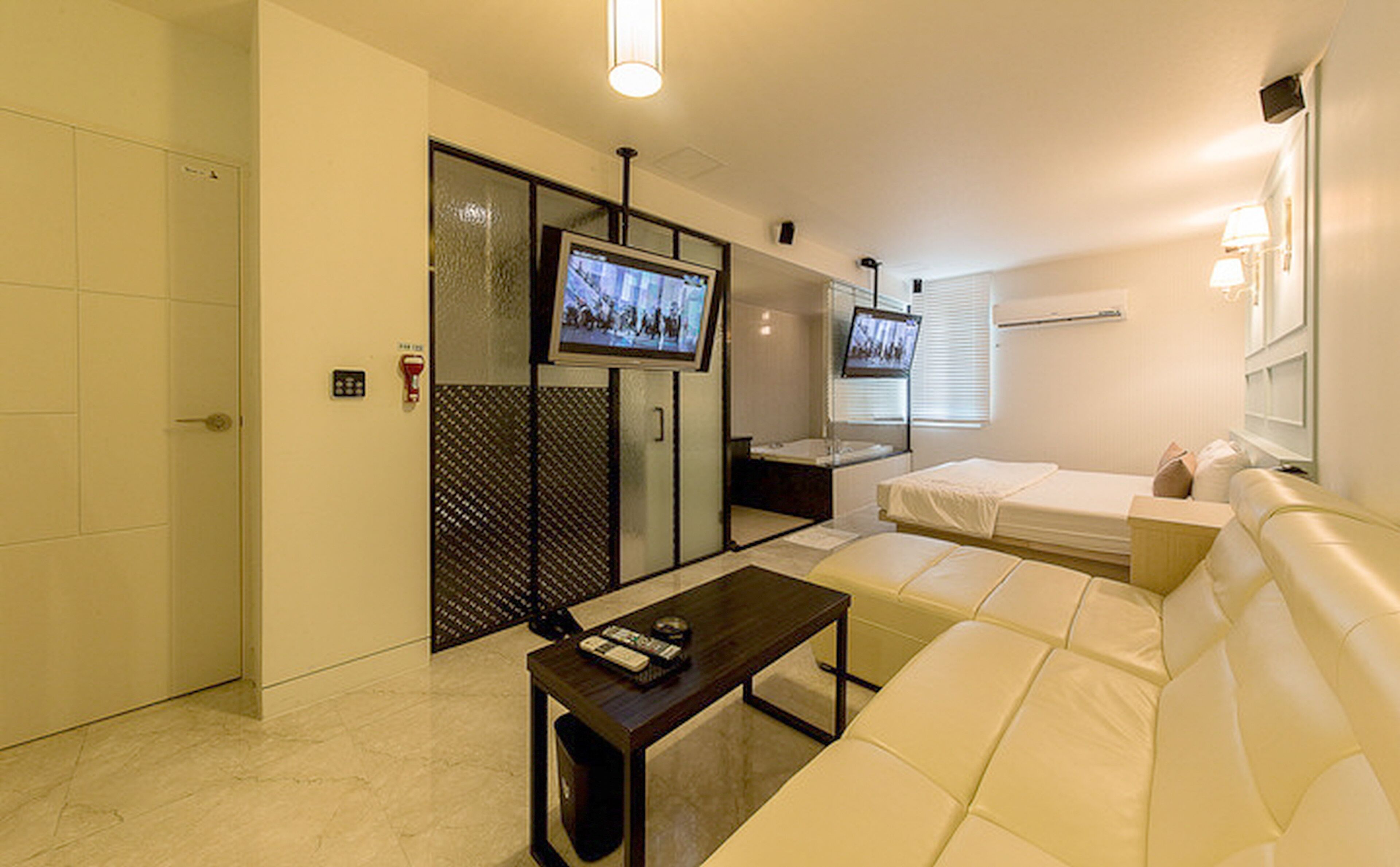 A hotel room with a sofa, a television, a small table, and a bathroom with a shower and toilet.