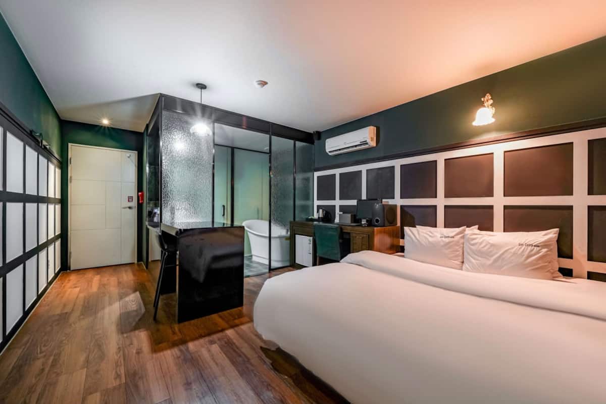 Moderni hotellihuone, jossa on suuri sänky, työpöytä, tuoli, vaatekaappi ja kylpyhuone.