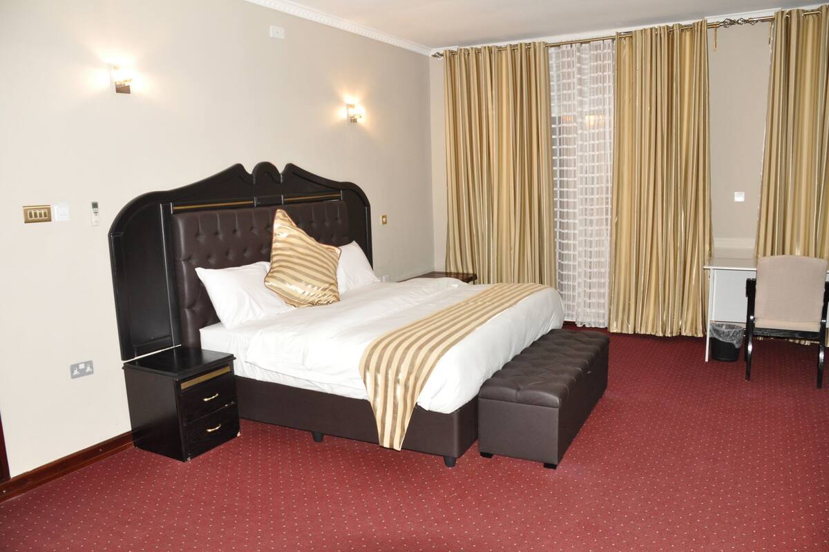 A hotel room with a large bed, a nightstand, a chair, and a desk.