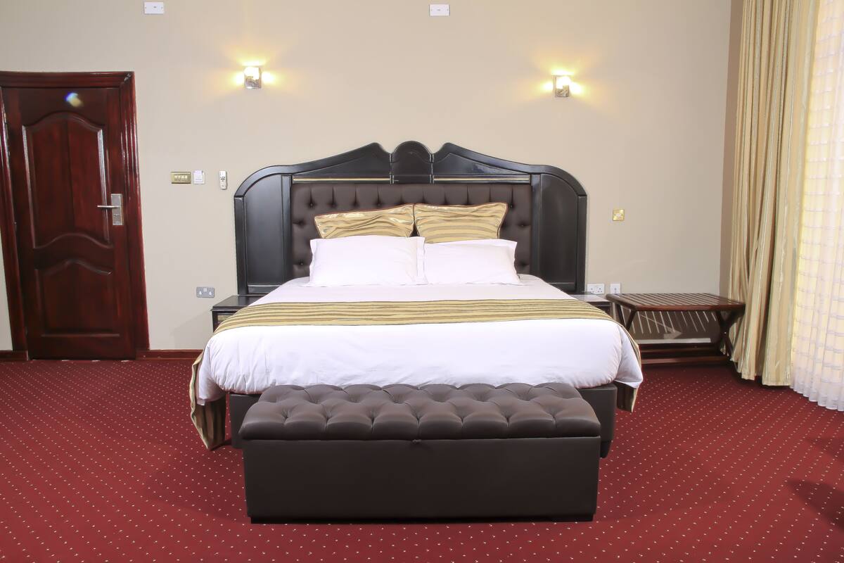 A neatly made bed with a dark headboard, white bedding, and two wall-mounted lights.