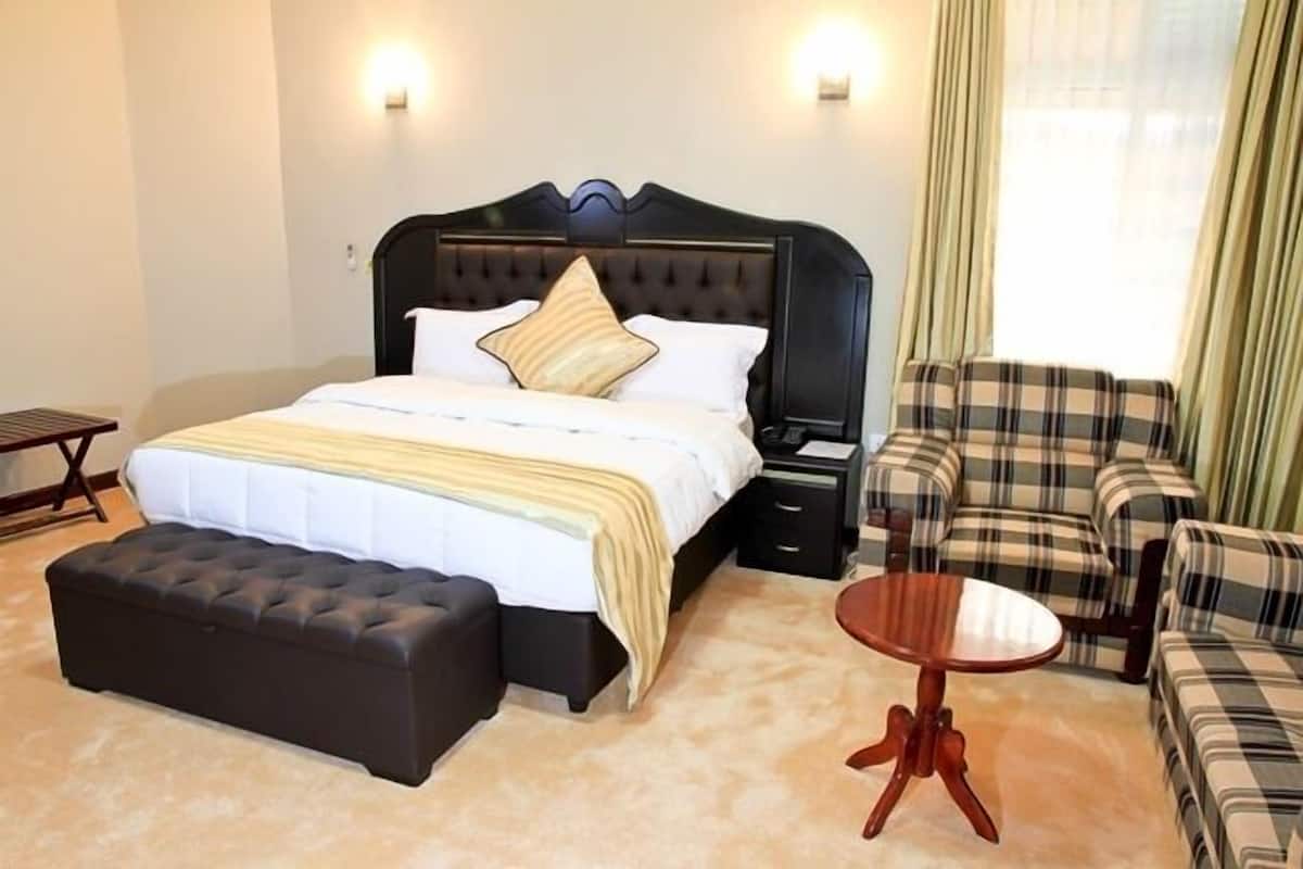 A neatly arranged hotel room with a large bed, a small round table, a sofa, and a bench.