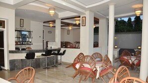 A restaurant with wicker chairs, a bar area, and a view of greenery outside. - New Agena Hotel (Bujumbura)