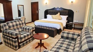 A hotel room with a large bed, two sofas, a small round table, a wardrobe, and a mirror. - New Agena Hotel (Bujumbura)