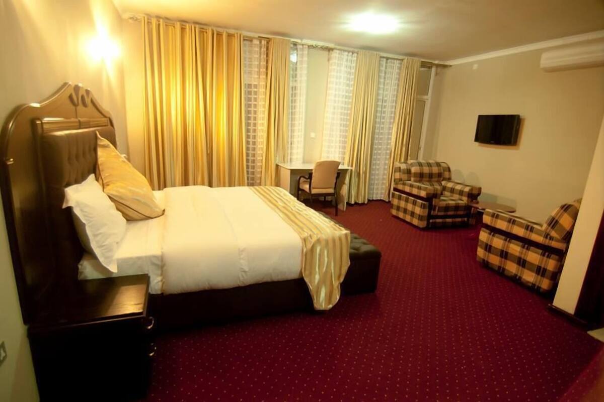 A hotel room with a large bed, a desk, a chair, and a television.