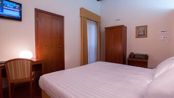 Una habitación de hotel con cama, escritorio, silla, televisor y armario.