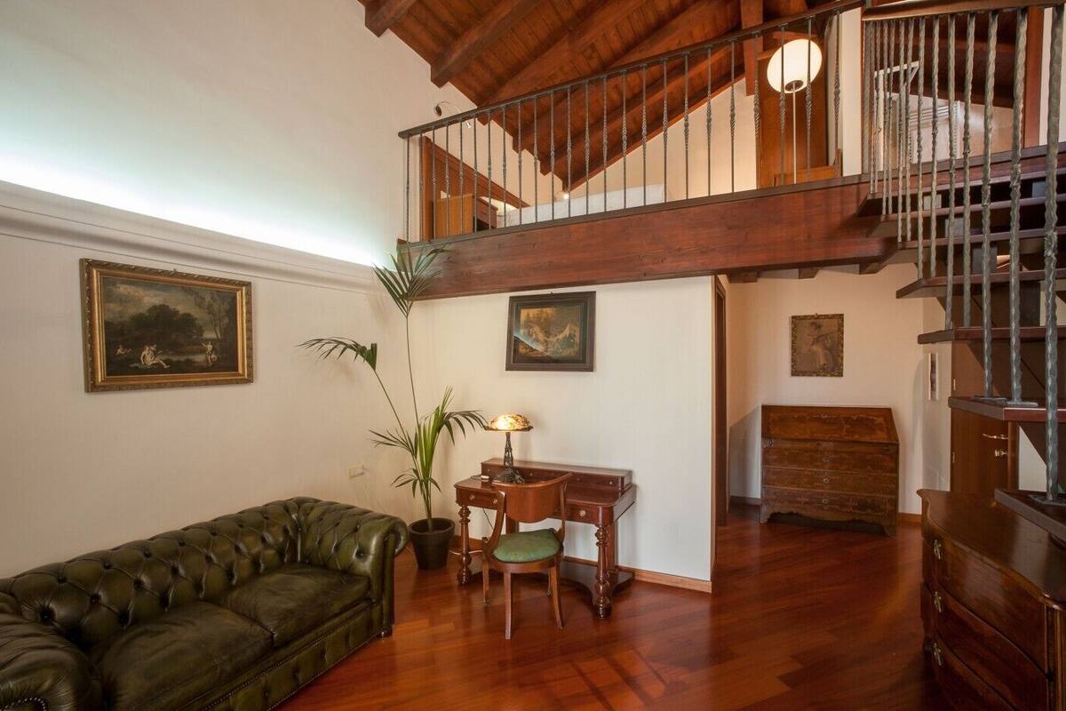 A spacious living room with a high ceiling, a wooden staircase, and a green leather sofa.