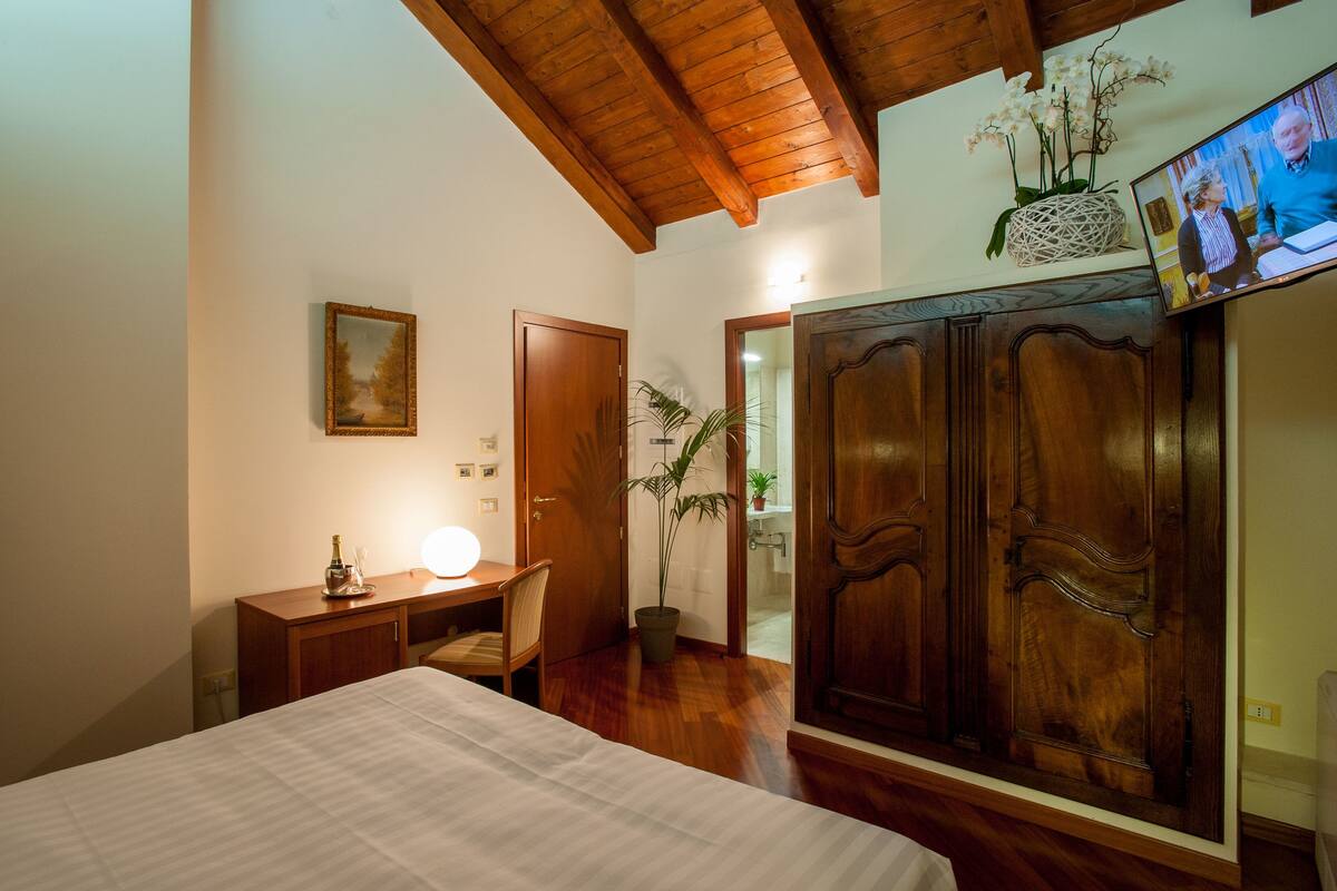 A bedroom with a bed, a desk with a lamp, a TV, and a wardrobe.
