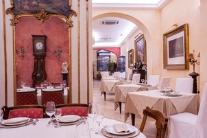 Un restaurante con mesas preparadas para comer, un reloj en la pared y obras de arte enmarcadas.