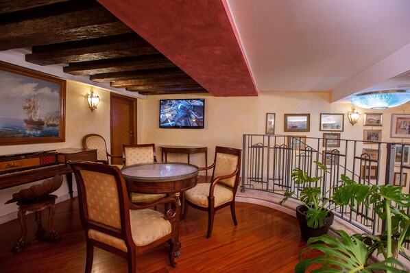 A dining area with a round table and chairs, a piano, and a television. - Hotel Flora (Cagliari)
