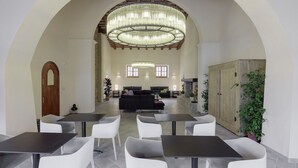 Amplio espacio interior con varias mesas y sillas, un gran candelabro y un aparador de madera.