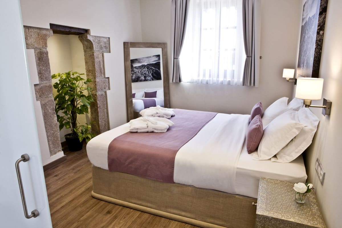 Ein Hotelzimmer mit Bett, Spiegel, Topfpflanze und einem Vorhangfenster.
