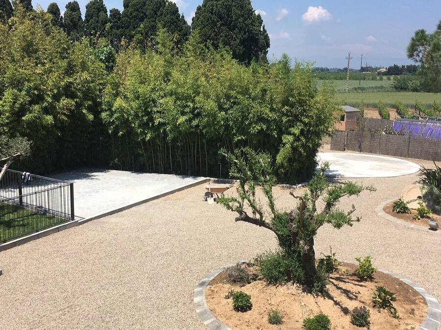 A landscaped outdoor area with a gravel path, a small tree, and a fenced area.