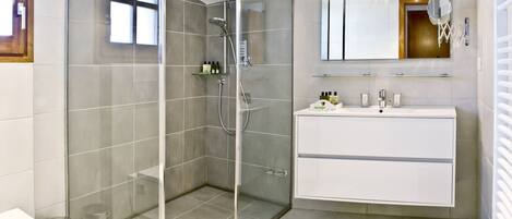 A modern bathroom with a glass-enclosed shower, a white vanity with a mirror, and a toilet.