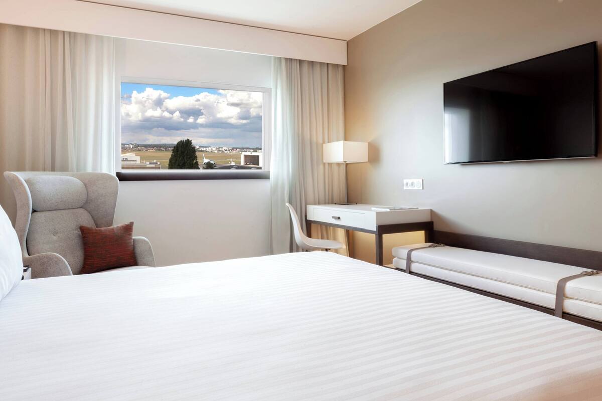 Une chambre d’hôtel avec un grand lit, un bureau, une chaise, une télévision et une fenêtre donnant sur la ville.