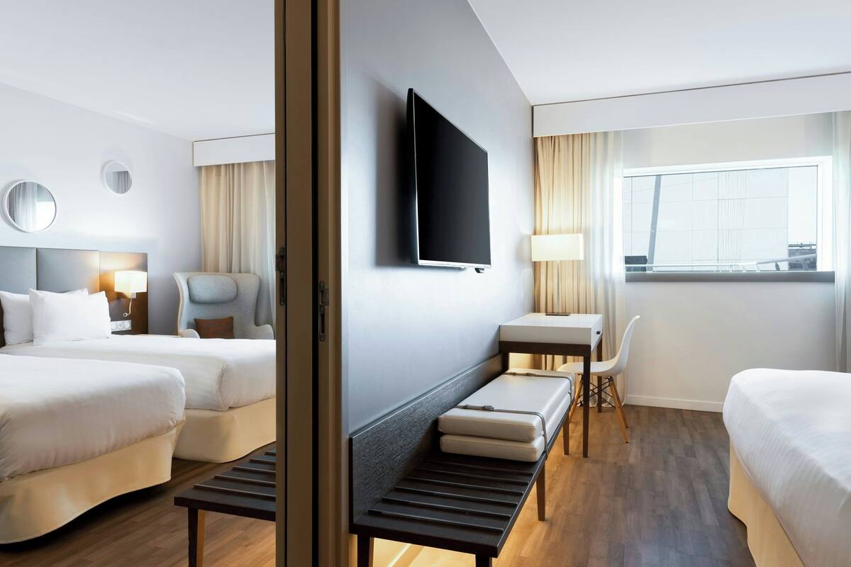 Une chambre d’hôtel avec deux lits, un bureau, une chaise, une télévision et une fenêtre avec des rideaux.