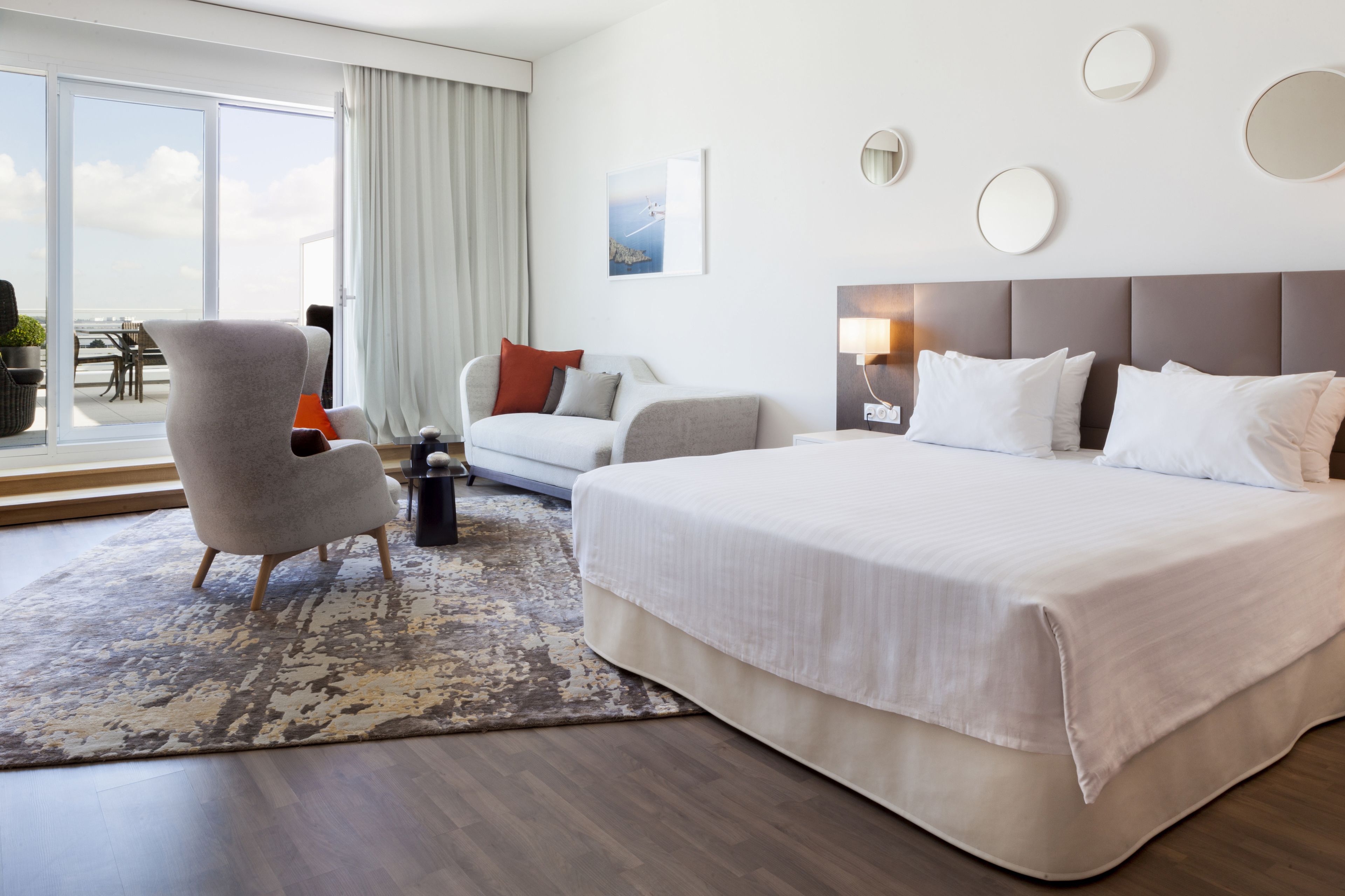 A hotel room with a large bed, a sofa, a chair, a small table, and a view of the outdoors.
