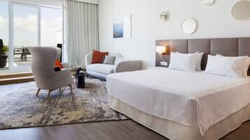 A hotel room with a large bed, a sofa, a chair, a small table, and a view of the outdoors.
