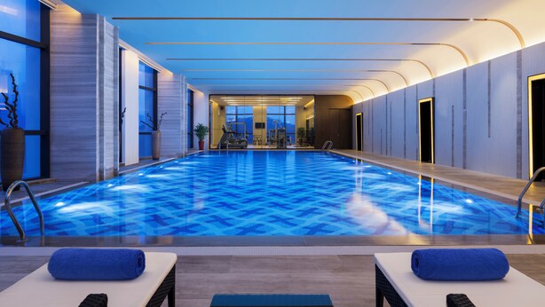 Una piscina interior con suelo de diseño azul, dos sillones de descanso con toallas azules y vistas a las montañas a través de las ventanas.