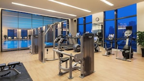 Uma academia com equipamentos de ginástica, piscina e amplas janelas com vista para a cidade.