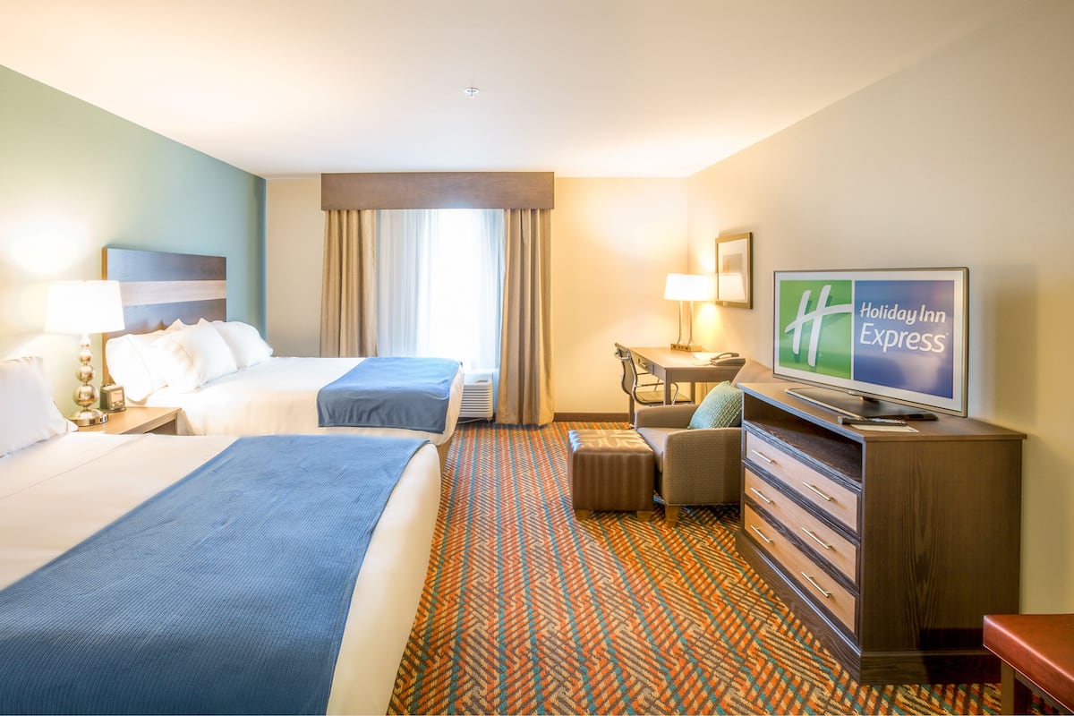 A hotel room with two beds, a desk, a television, and a patterned carpet.