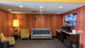 A lobby with a sofa, chairs, a desk, a lamp, and a wall-mounted TV. - Holiday Inn Express Wichita South by IHG (Wichita)