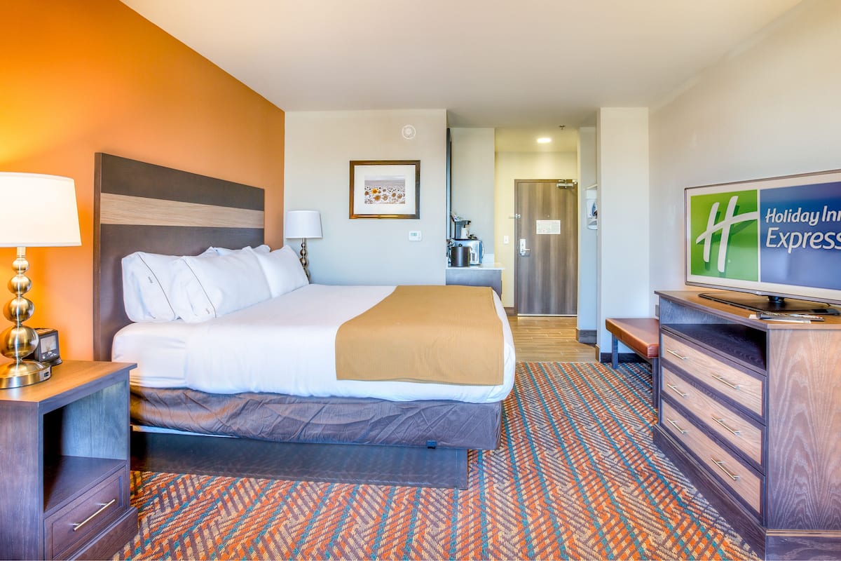 A hotel room with a bed, a desk, a television, and a coffee machine.