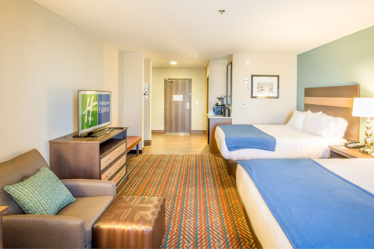A hotel room with a bed, a desk with a TV, a sofa, and a patterned rug.