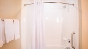 A shower area with a glass door, a towel rack with towels, and a handrail.