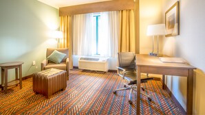 A hotel room with a bed, a desk, a chair, a table, an air conditioning unit, and a patterned carpet. - Holiday Inn Express Wichita South by IHG (Wichita)