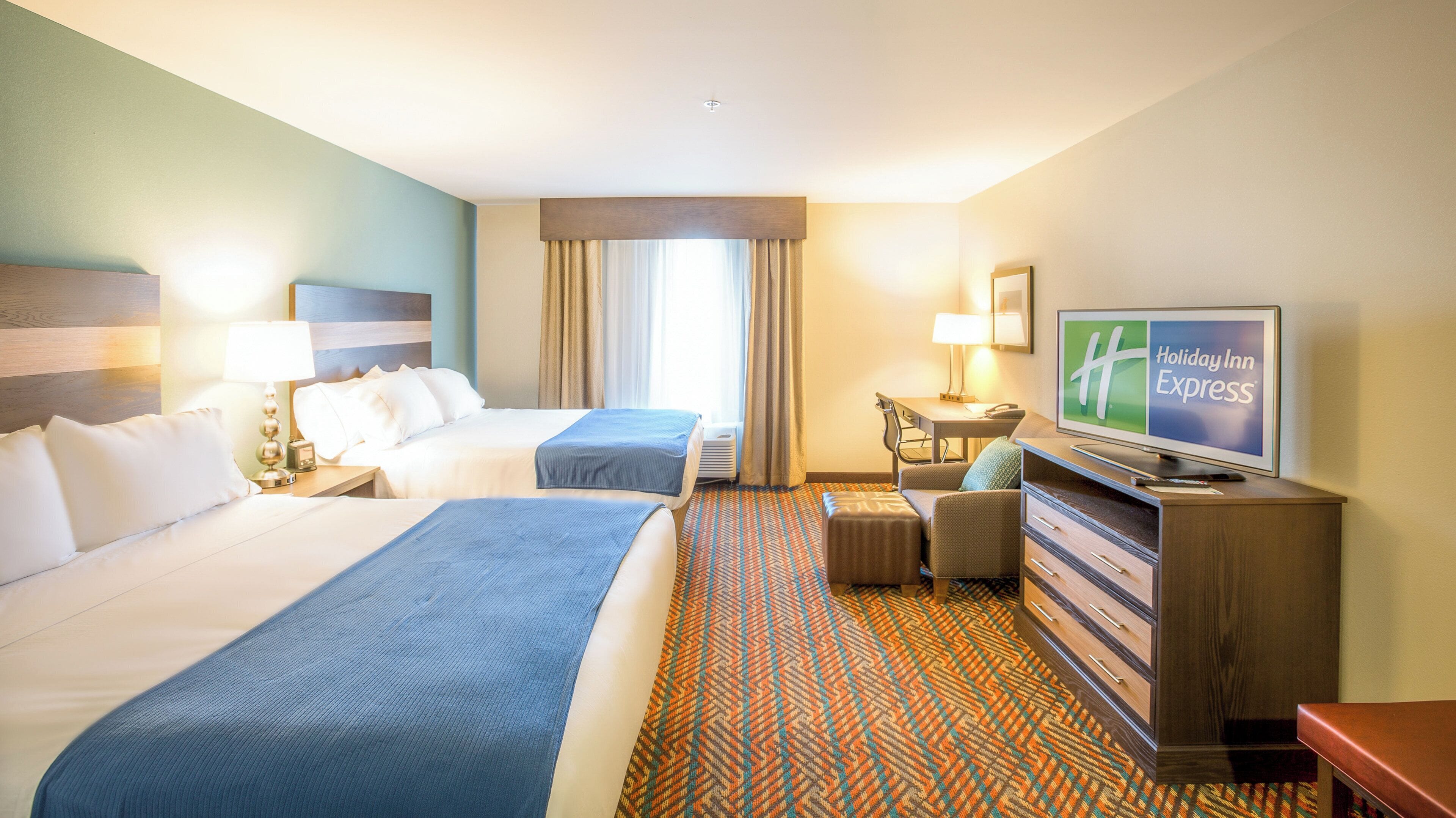 Une chambre d’hôtel avec deux lits, un bureau, une télévision et une moquette à motifs.