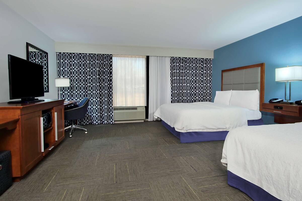 A hotel room with two beds, a desk with a TV, a desk lamp, and patterned curtains.