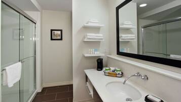 A modern bathroom with a glass shower enclosure, a white sink with a mirror above it, and shelves with towels.