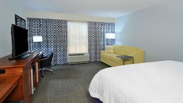 Ein Hotelzimmer mit einem Bett, einem Schreibtisch mit Fernseher, einem gelben Sofa und gemusterten Vorhängen.