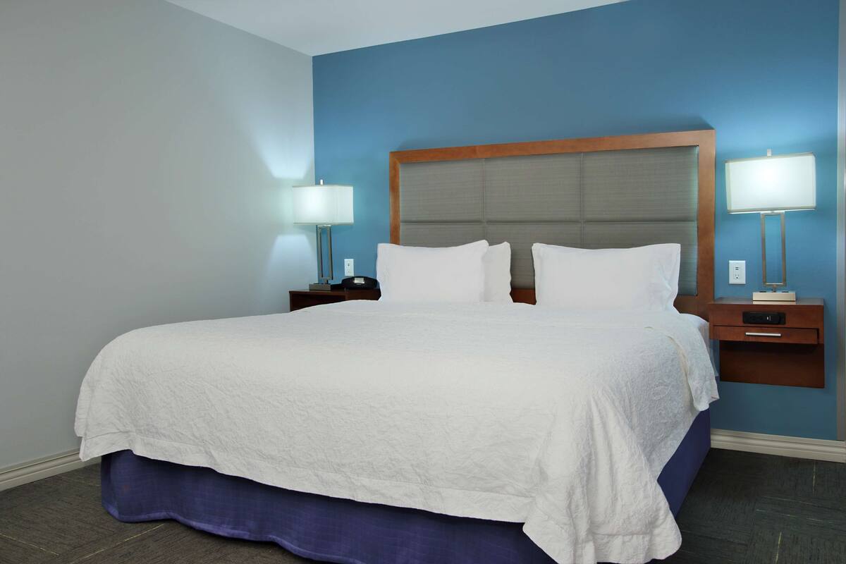 A neatly made bed with white linens, a wooden headboard, and two bedside tables with lamps.