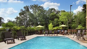 A rectangular swimming pool with lounge chairs and umbrellas, surrounded by a fence and trees. - Hampton Inn Richland (Richland)