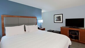 A hotel room with a large bed, a television, a nightstand with a lamp, and a microwave in a wooden cabinet. - Hampton Inn Richland (Richland)
