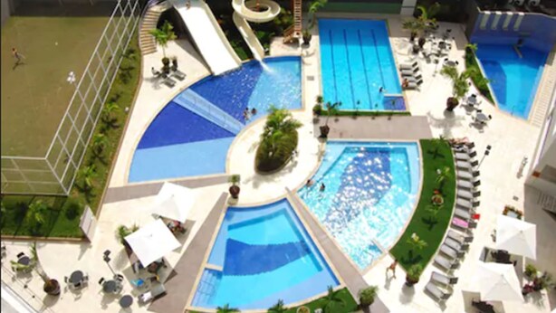 Area piscina sul tetto con diverse piscine, uno scivolo acquatico e lettini.
