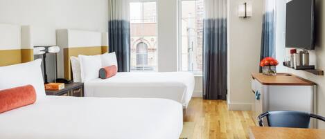 Habitación de hotel con dos camas, un escritorio, un televisor y vista a la ciudad.
