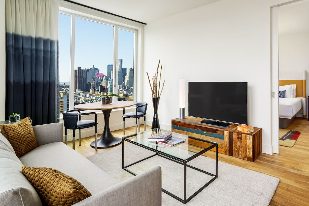 A modern living room with a sofa, coffee table, TV, and a city view through large windows.