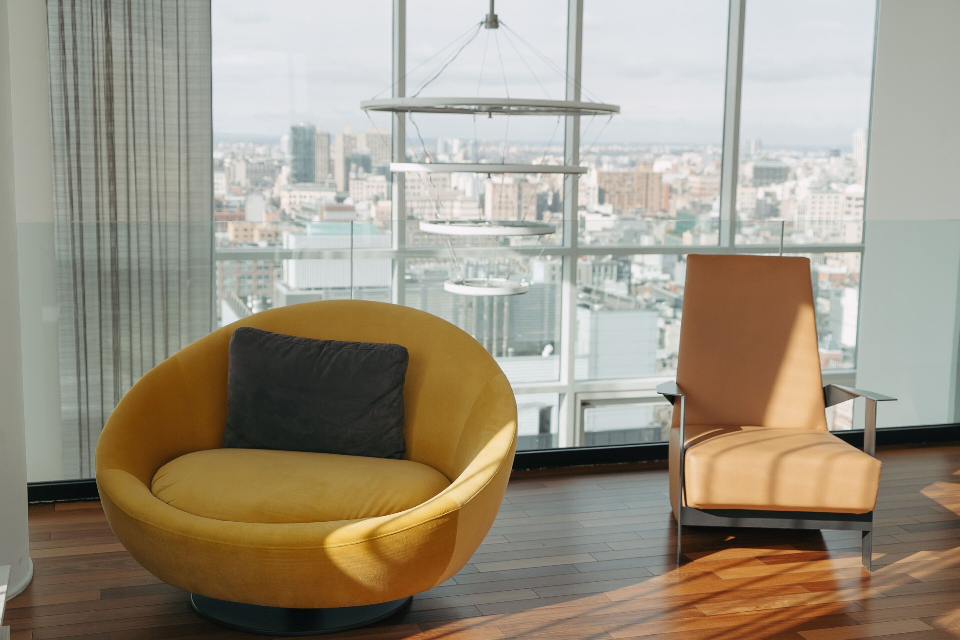 Una habitación moderna con un ventanal grande, una silla amarilla y una silla marrón.