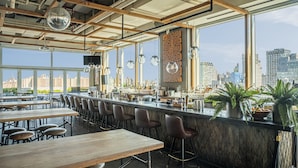 Een moderne bar met houten tafels en barkrukken, grote ramen met uitzicht op de stad, en hangende吊灯.