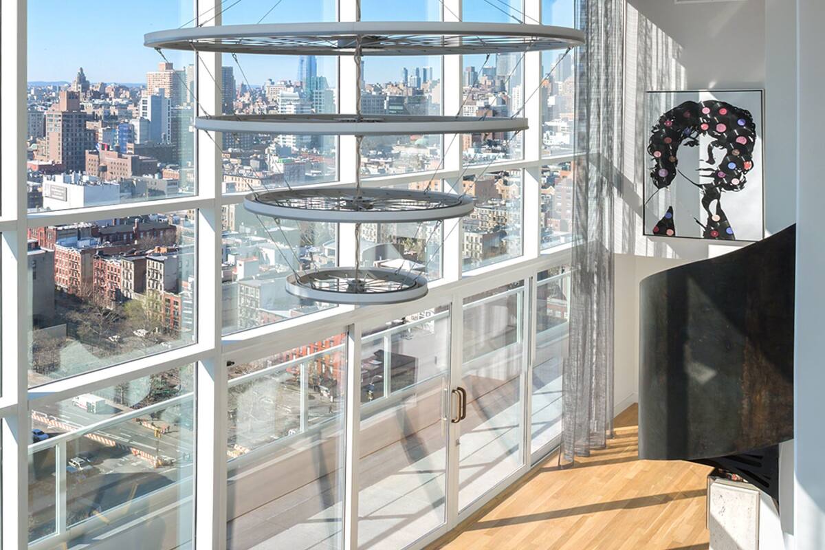A high-rise interior with large windows offering a city view, a modern circular light fixture, and a framed artwork on the wall.