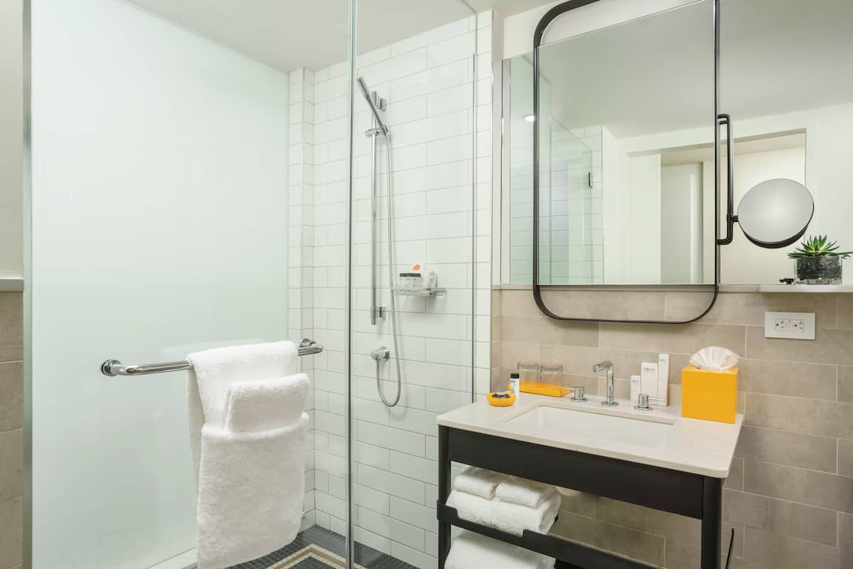 A modern bathroom with a glass shower enclosure, a white towel rack, a sink with a mirror, and a shelf with toiletries.