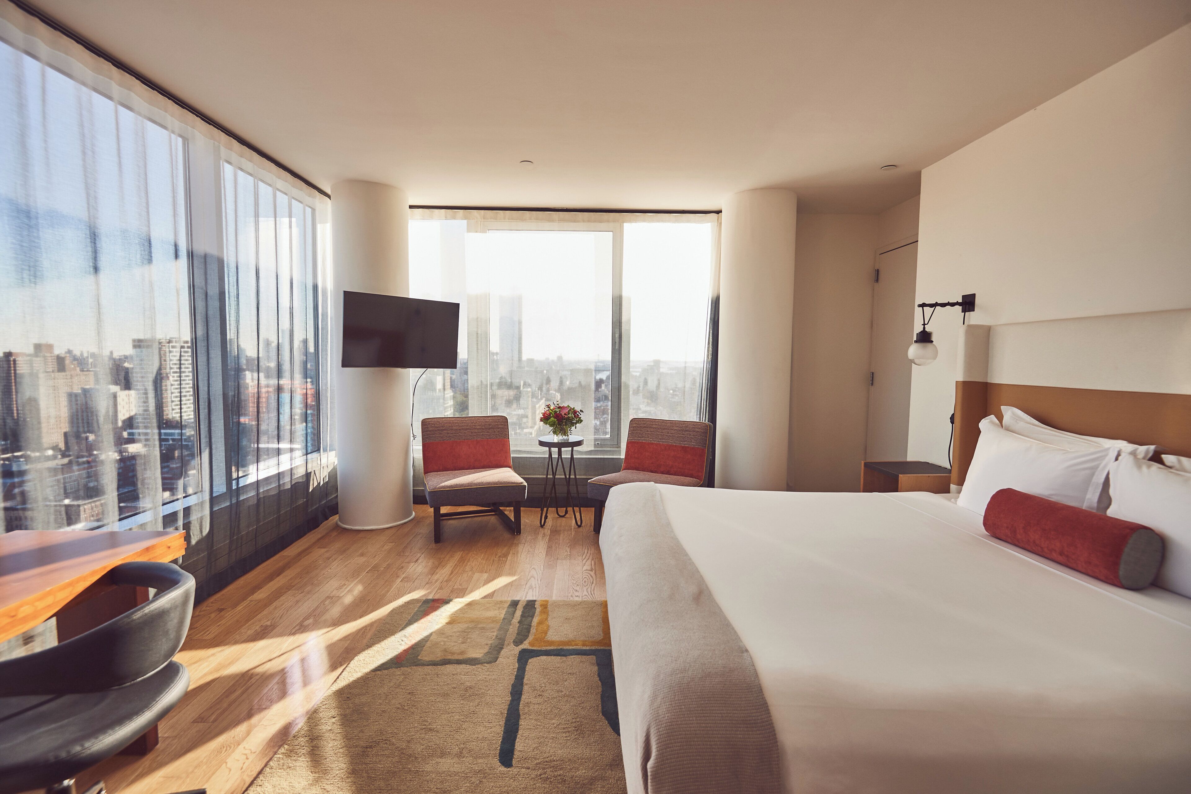 Une chambre d’hôtel avec un grand lit, un bureau, une chaise, une télévision et une vue sur le paysage urbain.