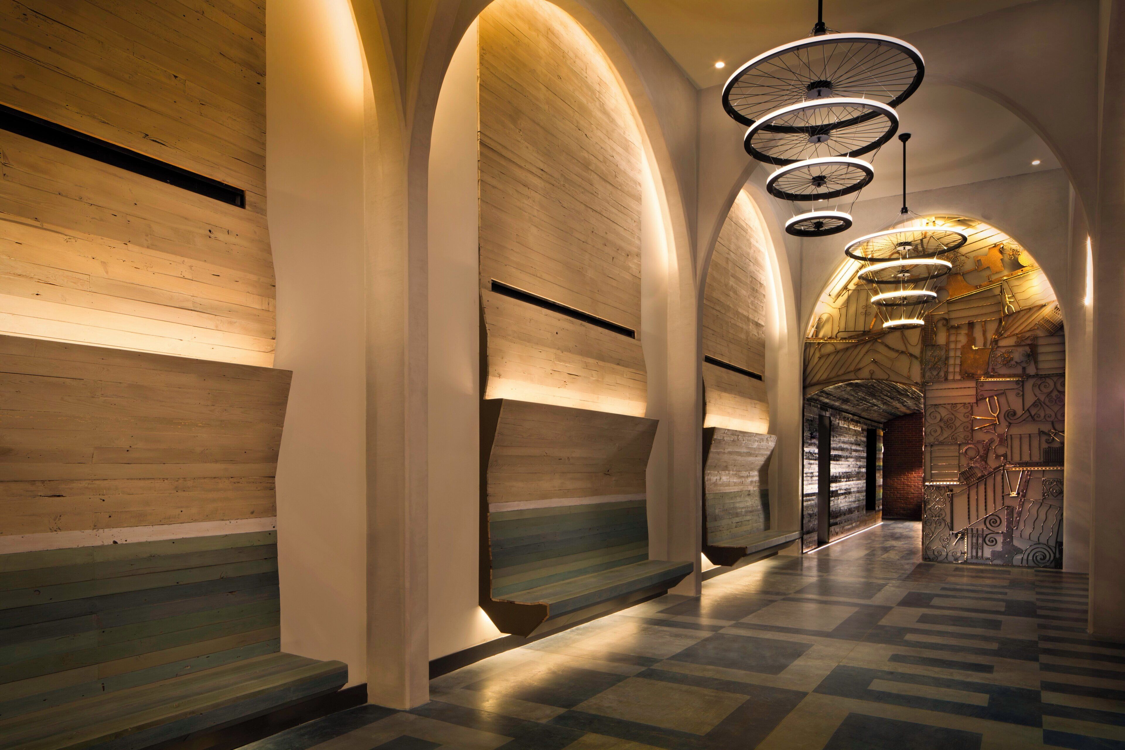 A corridor with wooden panel walls, a checkered floor, and a ceiling with circular light fixtures.